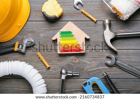 Model of house with builder's supplies and energy efficiency rating on wooden background Royalty-Free Stock Photo #2160734837