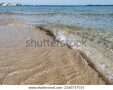 Protaras. Famagusta area. Cyprus. A small wave runs on the sandy shore of the beach in Fig Tree Bay against the background of the clear water of the Mediterranean Sea and the blue cloudless sky.
