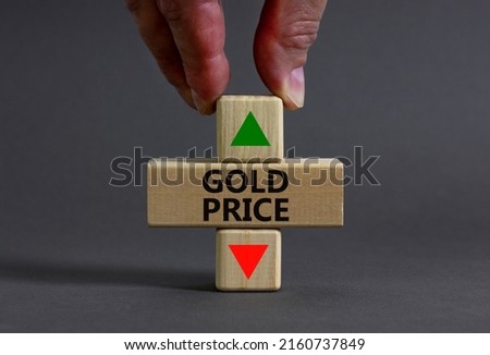 Gold price symbol. Businessman holds a wooden cube with arrow symbolizing that Gold price are going down or up. Beautiful grey table grey background. Business and gold price concept. Copy space.