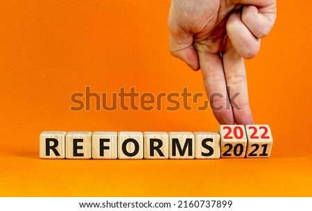 2022 reforms new year symbol. Businessman turns a wooden cube and changes words 'reforms 2021' to 'reforms 2022'. Beautiful orange background, copy space. Business, 2022 reforms new year concept.