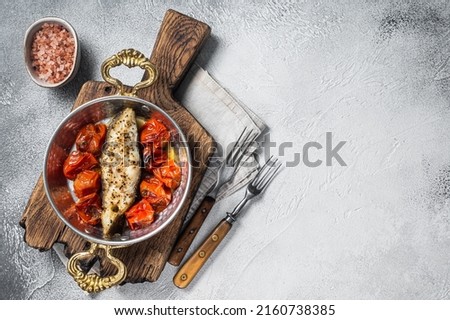 Fried halibut fish steaks with tomato in skillet. White background. Top view. Copy space.
