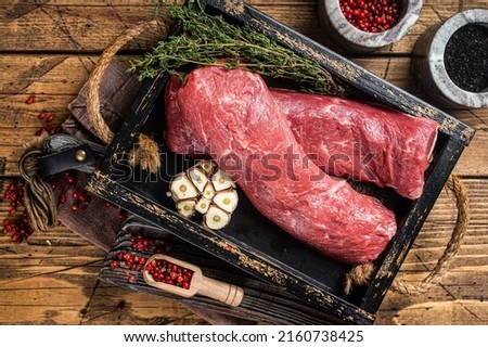 Lamb tenderloin fillet for steaks, uncooked meat in wooden tray with herbs. Wooden background. Top view.