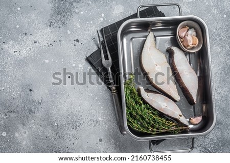 Fresh steak of raw fish halibut in kitchen tray with herbs. Gray background. Top view. Copy space.