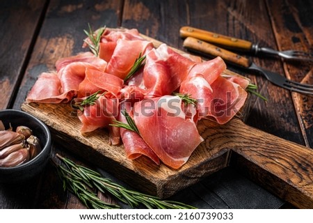 Slices of jamon serrano ham or prosciutto crudo parma on wooden board with rosemary. Wooden background. Top view. Royalty-Free Stock Photo #2160739033