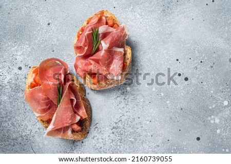 Spanish Tapas with tomatoes and cured Slices of jamon iberico ham, fresh toasts. Gray background. Top view. Copy space. Royalty-Free Stock Photo #2160739055