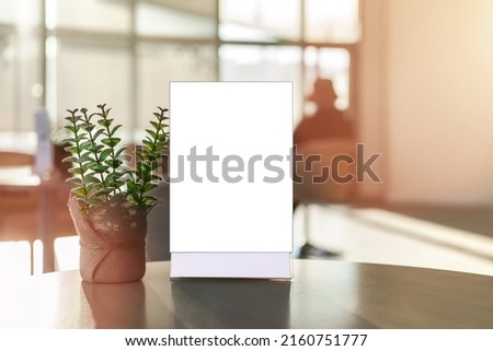Empty menu holder in plastic frame stands on wooden cafe table with flowerpot indoor. Food industry and business concept.