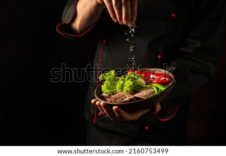The chef sprinkles salt on a sliced steak with beef and vegetables in a plate. The concept of serving dishes to order.