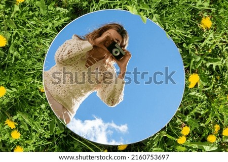 photography and nature concept - woman with camera and sky reflection in round mirror on grass