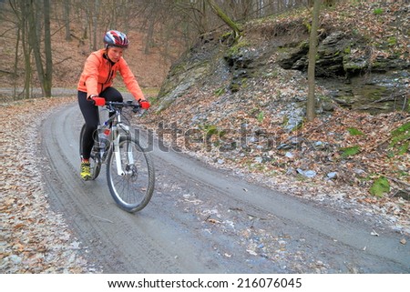 Woman pedaling on a mountain bike descends a forest road in overcast day