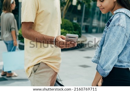 Unrecognizable Man Showing Mobile Phone To His Female Friend Outdoors. 
Close up photo of man hand using smartphone while he standing at city street with a cute teenager girl. Royalty-Free Stock Photo #2160769711