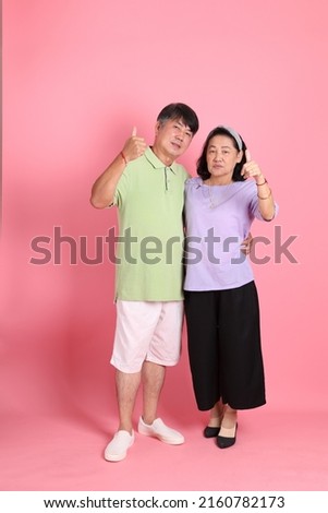 The senior Asian couple with casual clothes standing on the pink background.