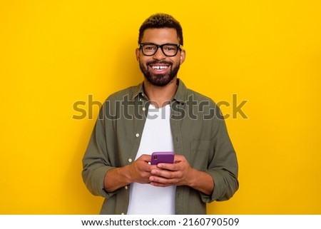Photo of positive attractive guy dressed green shirt eyewear communicating modern gadget isolated yellow color background