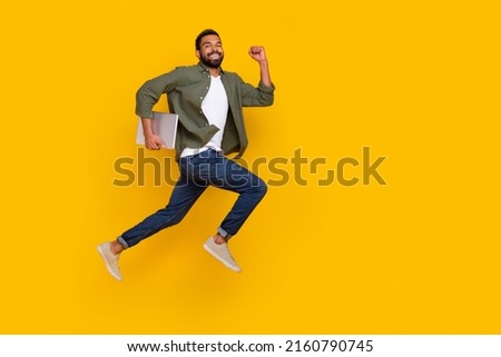 Full length photo of cute funky guy dressed green shirt jumping running modern gadget empty space isolated yellow color background Royalty-Free Stock Photo #2160790745