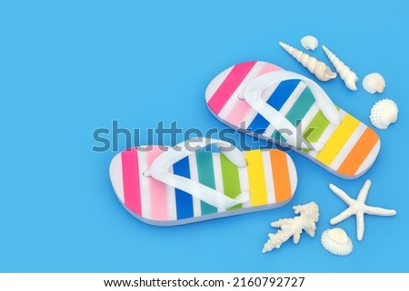 Summer rainbow striped flip flops on blue background with seashells. Trendy footwear for beach holiday vacation and LGBT themed concept. Copy space, top view.