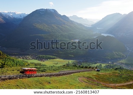 A red funicular carriage climbs up the slope towards Muottas Muragl, overlooking Pontresina and St Motritz villages and lakes in Engadin Valley under alpine mountains, in Samedan, Grisons, Switzerland Royalty-Free Stock Photo #2160813407