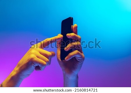 Touch phone screen. Closeup male hands holding gadget, smartphone isolated on gradient blue and purple background in neon. Concept of mobile lifestyle, digital technology, social gathering.