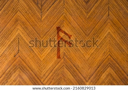Close-up shot of a wooden surface with a Norse rune engraved on it, especially the Ansuz character