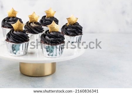 Black cupcakes decorated with a gold star on a cake stand