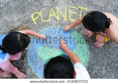 Volunteer family paints a beautiful world with the message Planet on asphalt. Little children and young woman drawing with colorful chalk on courtyard. Concepts of world environment day and peace day.