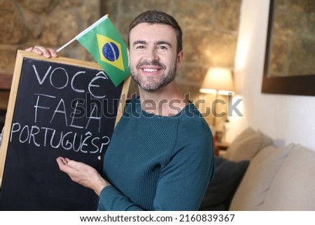 Portuguese teacher holding blackboard and Brazilian flag. TRANSLATION OF THE TEXT IN THE IMAGE: "Do you speak Portuguese?" Royalty-Free Stock Photo #2160839367