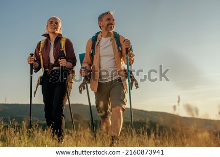 Hiking middle age couple follow trail along grassy mountain ridge Royalty-Free Stock Photo #2160873941