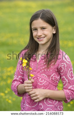 Girl with wild flowers in field, smiling, portrait