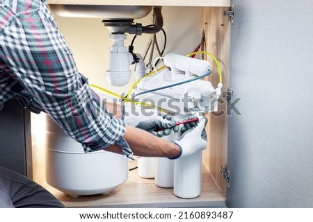 Plumber hand in gloves replace water filter cartridges at kitchen. Fix purification osmosis system. Technician installing or repairing system of water filtration. Royalty-Free Stock Photo #2160893487
