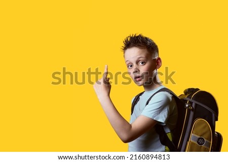 A first-grader schoolboy back to school in September with a backpack and textbooks on a yellow background, autumn concept