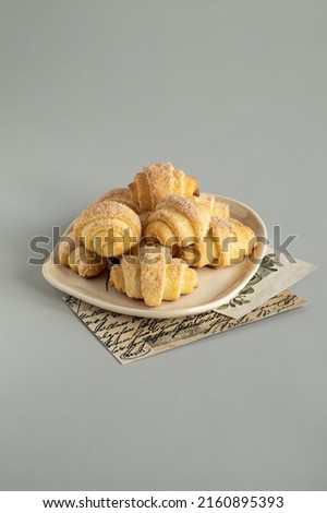 Mini cottage cheese croissants. Bagels with sugar on the milky color ceramic plate. Vintage paper pictures