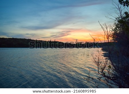 Sunset over a lake in Texas at Cleburne State Park. Room for text or copy space. Blue background with red, orange, and yellow towards the right side of the picture.