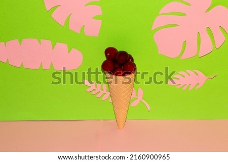 ice cream with cherries in a cone on a pink-green background with jungle leaves pink, creative summer design. tropical wallpaper