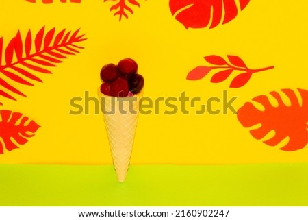 cherry in a cone on a yellow-green background, creative summer health design, ice cream health, jungle leaves
