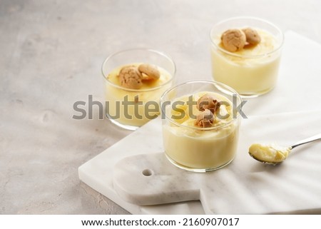 Creamy french vanilla pudding in glass decorated with italian biscuits amaretti on marble board on grey neutral background