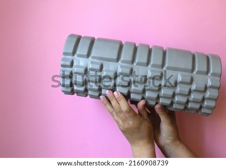 a woman's hand holds a gray massage roll on a pink background