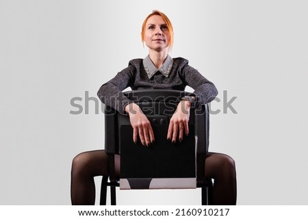 Business woman, legs wide apart, sits on a chair backwards, on a gray background. High quality photo