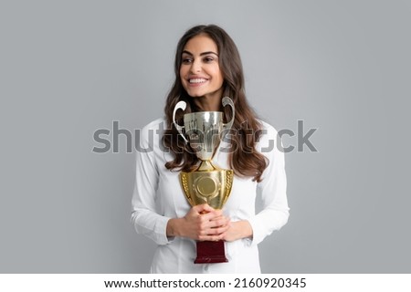 Cheerful businesswoman holding trophy standing posing on grey background. Successful employee holds winner cup. Award ceremony for winner. Best manager. Royalty-Free Stock Photo #2160920345