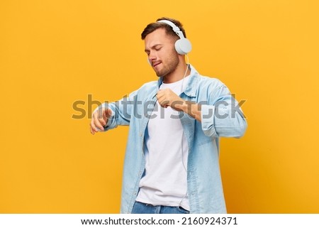 Overjoyed tanned handsome man in blue basic t-shirt headphones move on favorite playlist posing isolated on orange yellow studio background. Copy space Banner Mockup. Time to relax concept