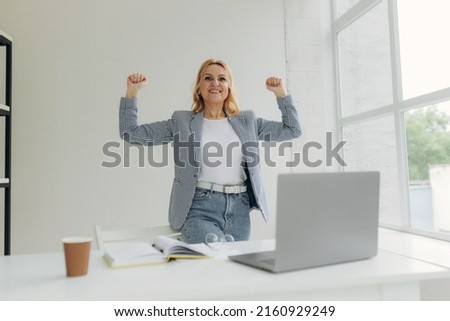 Portrait of excited mature woman celebrating success in office and looking at computer screen