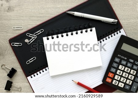 An open notebook with blank pages, a pen and a calculator on a wooden table. view from above