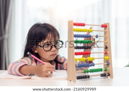 A young cute Asian girl is using the abacus with colored beads to learn how to count at home Royalty-Free Stock Photo #2160929989