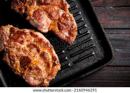 Grilled pork steak in a frying pan. On a dark wooden background. High quality photo