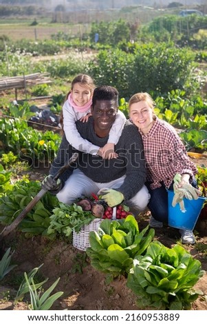 Happy family couple of gardeners with daughter holding harvest of fresh vegetables in garden on a sunny spring day