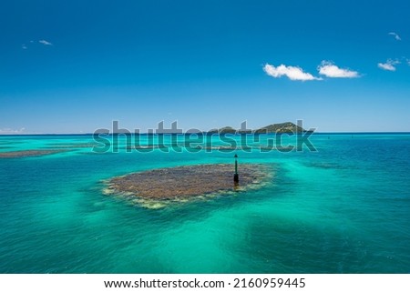 Seascape photo of remote island of Mangareva in the Gambier Archipelago of French Polynesia, South Pacific, blue sky with coral reef in turquoise waters and volcanic mountains in the background