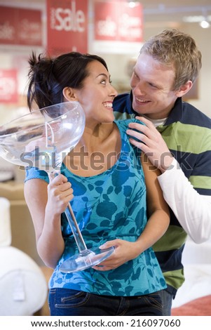 Young woman with giant cocktail glass in shop, smiling at man