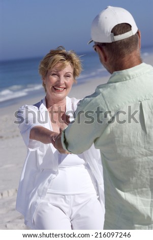 Senior couple holding hands on beach, smiling at each other