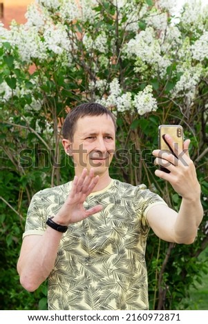 Portrait of attractive adult man with smartphone, looking at picture on mobile phone, smiling. Video communication concept. Father's Day, selective focus Natural background, using technology outdoors