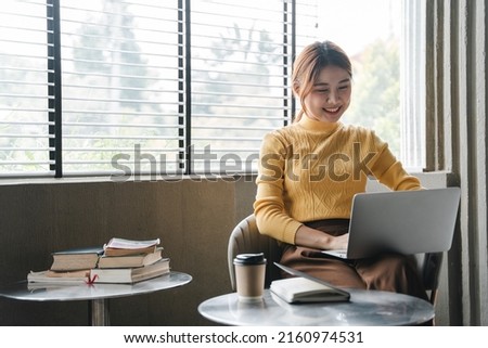 Asian girl. Beautiful woman enjoys chatting on her laptop on the phone in the house next to the window.