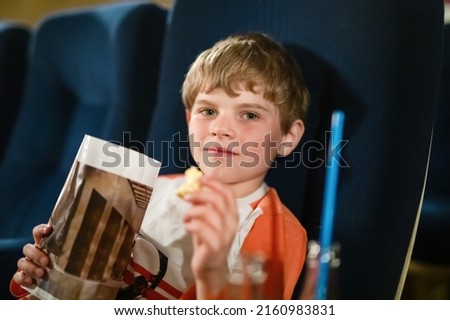 Cute school boy watching cartoon movie in the cinema. Leisure and activity for family with kids. Happy child with popcorn.