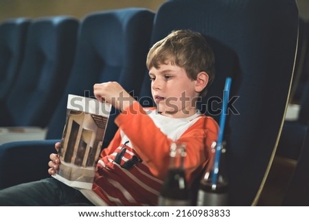 Cute school boy watching cartoon movie in the cinema. Leisure and activity for family with kids. Happy child with popcorn.
