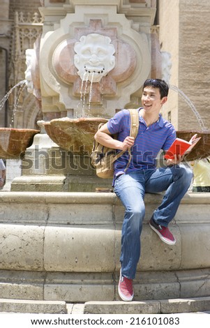 Man on edge of fountain with book, smiling